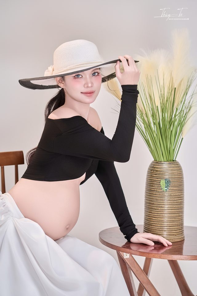 Mom ngồi ghế bên bình cỏ, mũ vành rộng
